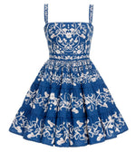 The Lima Mini Dress by Agua By Aguabendita is a sleeveless blue cotton mini dress with a fitted bodice, flared skirt, white floral embroidery, tiered layers, and signature Lima Ribbons detail.