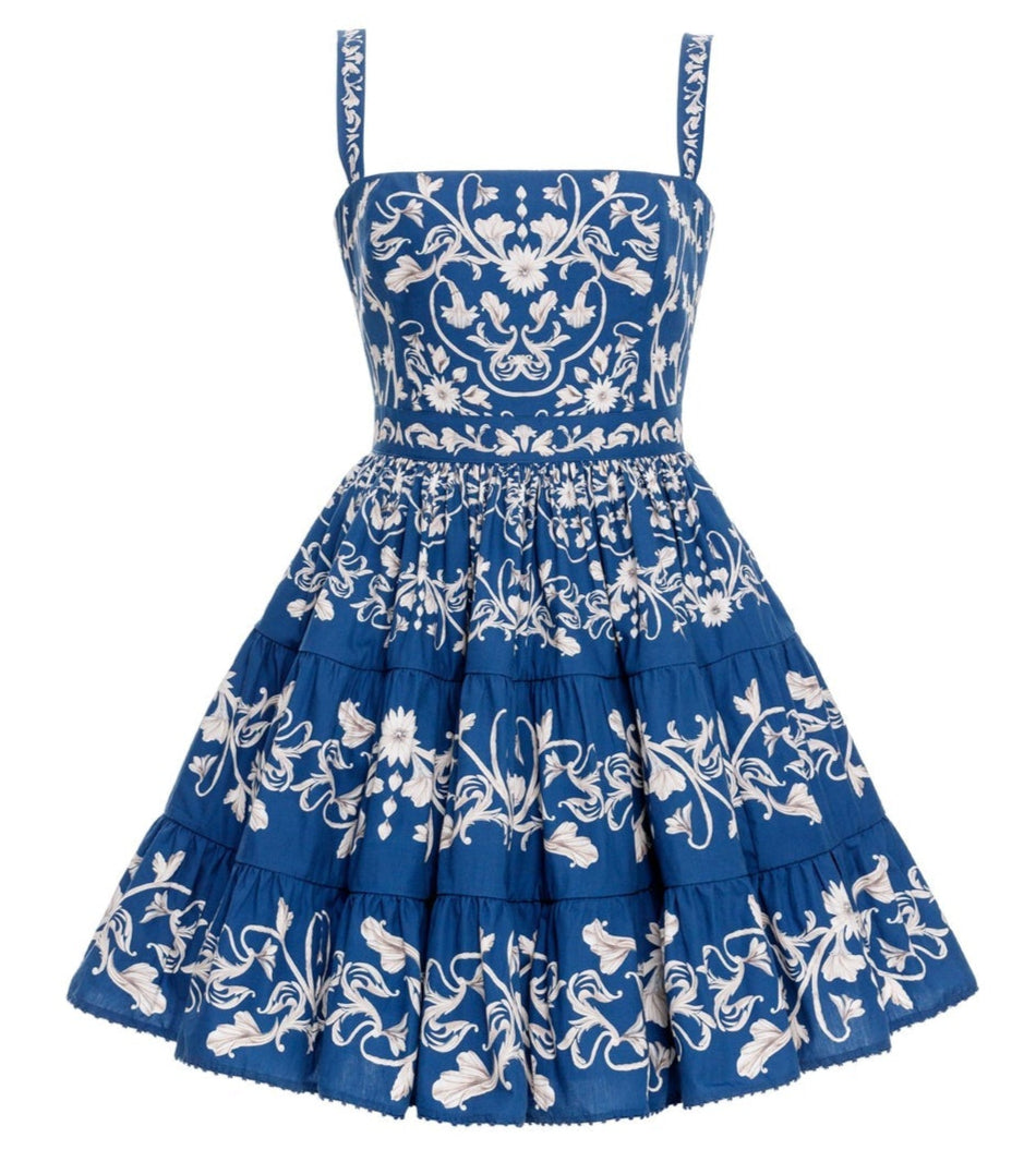 The Lima Mini Dress by Agua By Aguabendita is a sleeveless blue cotton mini dress with a fitted bodice, flared skirt, white floral embroidery, tiered layers, and signature Lima Ribbons detail.
