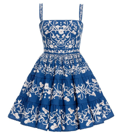 The Lima Mini Dress by Agua By Aguabendita is a sleeveless blue cotton mini dress with a fitted bodice, flared skirt, white floral embroidery, tiered layers, and signature Lima Ribbons detail.