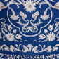 Close-up of blue fabric from the Lima Mini Dress by Agua By Aguabendita, featuring intricate white floral embroidery and pleated detailing at the hem.
