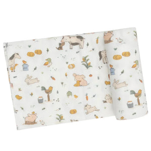 The Angel Dear Farm Babies Swaddle Blanket is a cuddly, rolled-up baby blanket showcasing a charming design with farm animals and vegetables such as cows, rabbits, pumpkins, and carrots on a white background. It's perfect for swaddling and adds a delightful touch to any nursery.