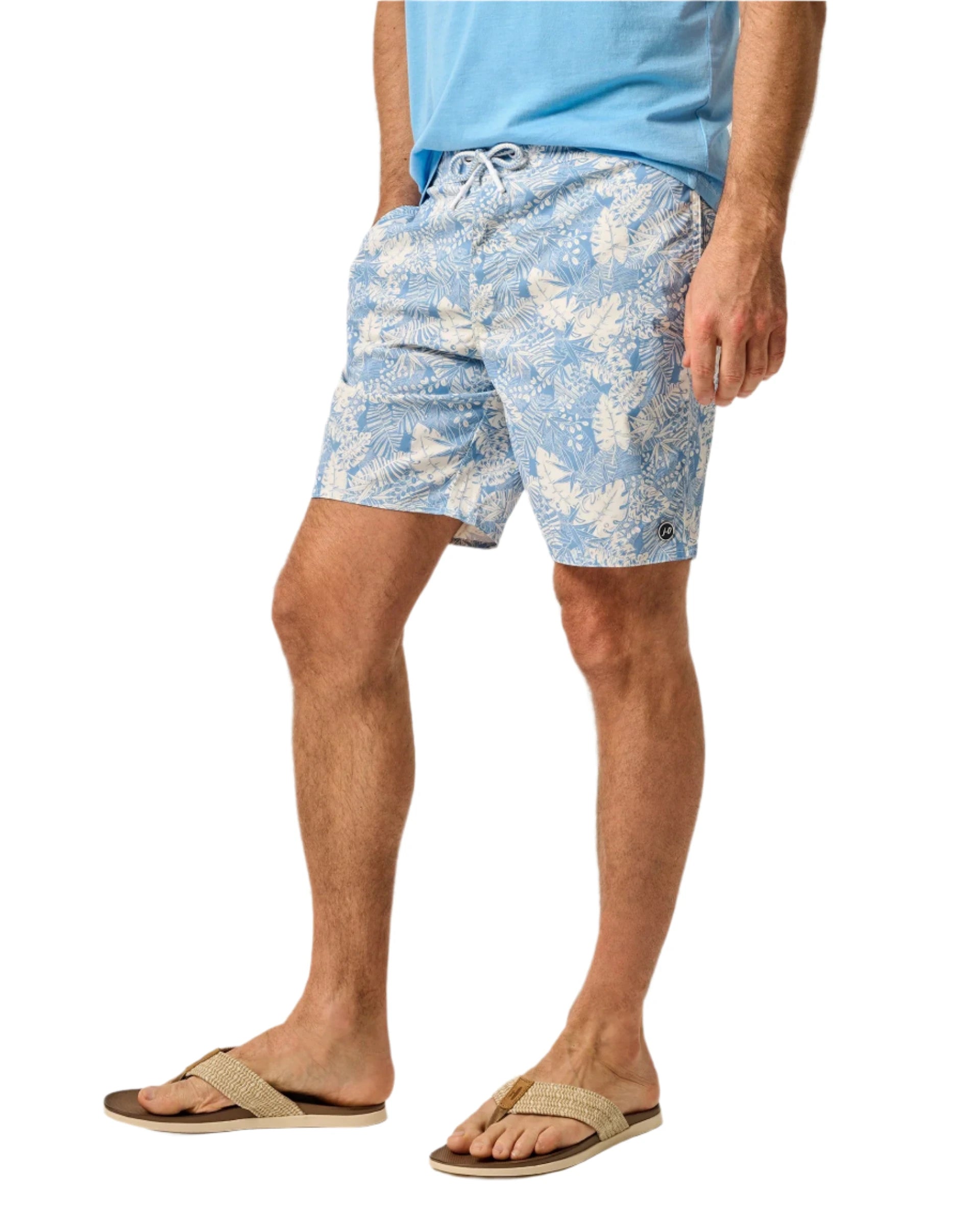 A man in a light blue shirt and Johnnie-O Salty Dogs Swim Trunks stands with one hand in his pocket, rocking casual flip-flops.