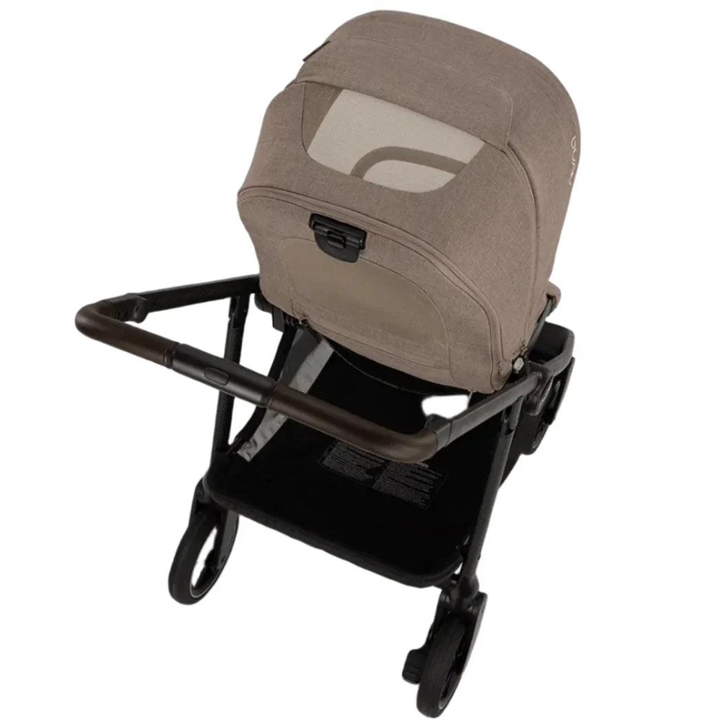 The Nuna SWIV Stroller by Nuna is a brown baby stroller with a closed canopy and a mesh window on the back for ventilation, mounted on a black frame with four 360-degree swivel wheels.