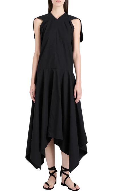 A woman models the Proenza Schouler Sybella Dress, a sleeveless black design with a handkerchief hem and flowing silhouette, paired with black lace-up sandals against a white background.
