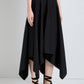 A person wearing the Sybella Dress by Proenza Schouler, featuring a black handkerchief hem and flowing silhouette, pairs it with black strappy sandals and stands against a plain light-colored background.
