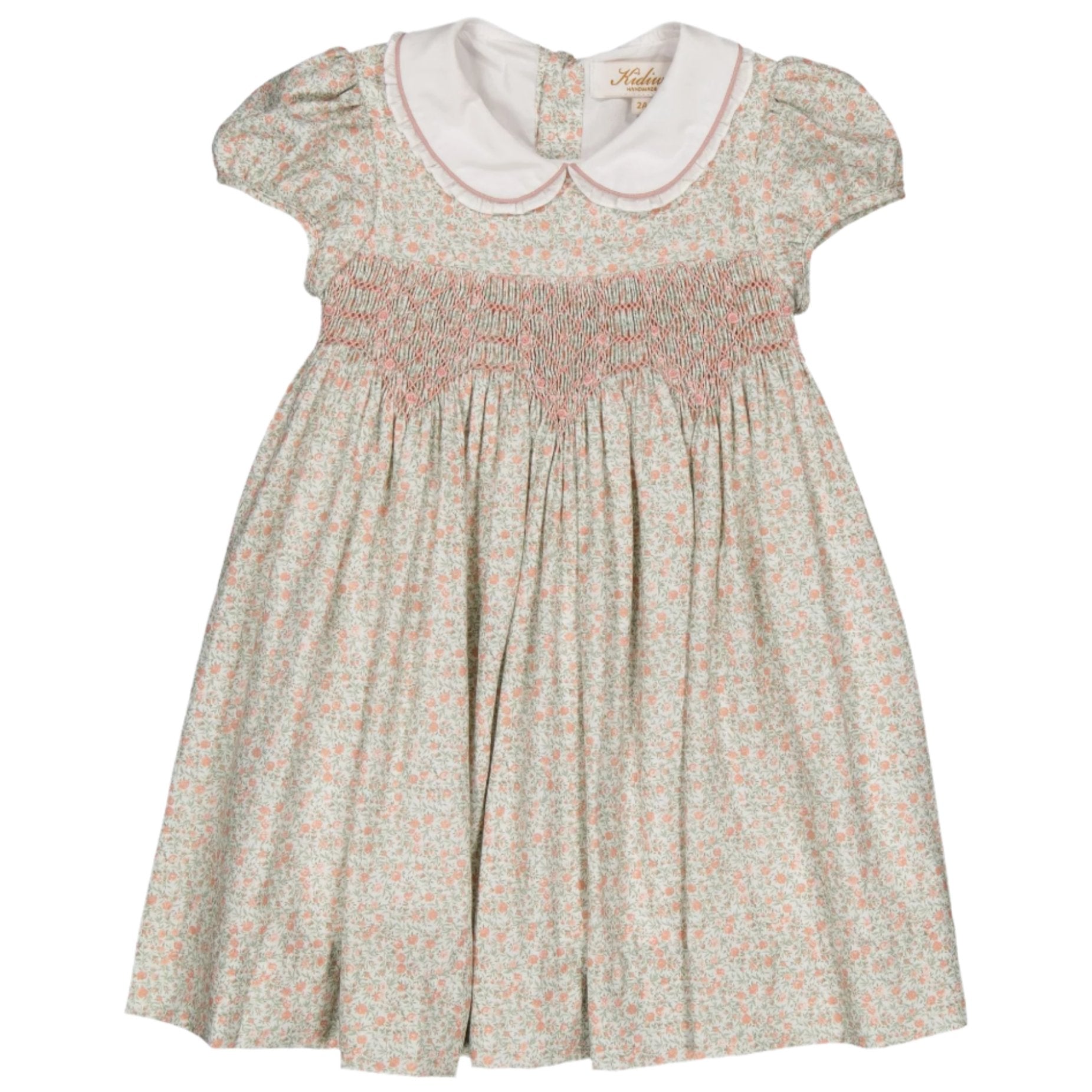 The Kidiwi Sybelle Smocked Dress showcases a delightful floral design, complete with a white Peter Pan collar and vibrant hot pink smocking on the bodice. Crafted from BCI certified cotton, it brings eco-friendly elegance to your wardrobe.