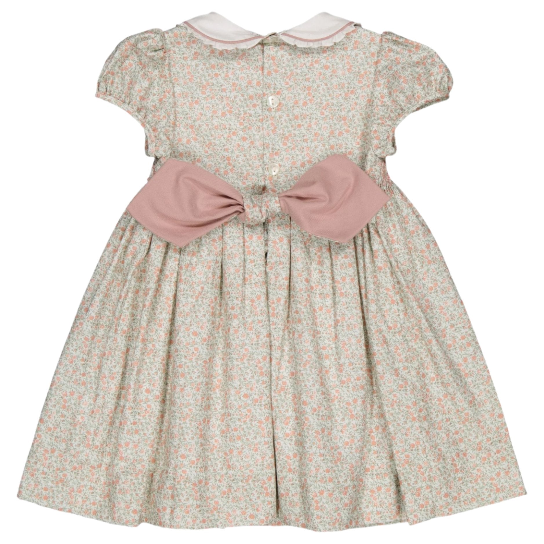 The Kidiwi Sybelle Smocked Dress showcases a delightful floral design complemented by an adorable pink bow at the back. Crafted from BCI certified cotton, this baby dress ensures both comfort and style with its short sleeves, making it ideal for any occasion.