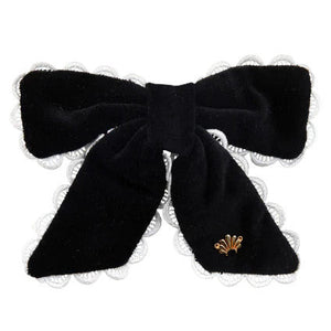 The Beaufort Bonnet Company’s T.B.B.C. x Lele Sadoughi Britney Barrette features black velvet, white lace trim, and a gold emblem, blending classic and elegant style reminiscent of Lele Sadoughi accessories.