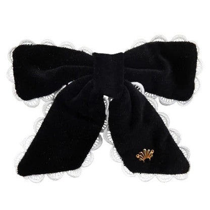 The Beaufort Bonnet Company’s T.B.B.C. x Lele Sadoughi Britney Barrette features black velvet, white lace trim, and a gold emblem, blending classic and elegant style reminiscent of Lele Sadoughi accessories.