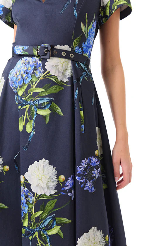 Person wearing a Monique Lhuillier Short Sleeve A Line Printed Poplin Dress with a floral pattern of white, blue, and green flowers, featuring a belted waist.