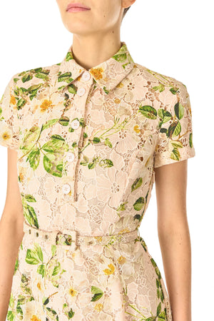 A woman wears the Monique Lhuillier Lace Polo Shirt Dress with short sleeves, button-up front, guipure lace, green leaves, yellow flowers, matching belt, and a tea-length A-line skirt.