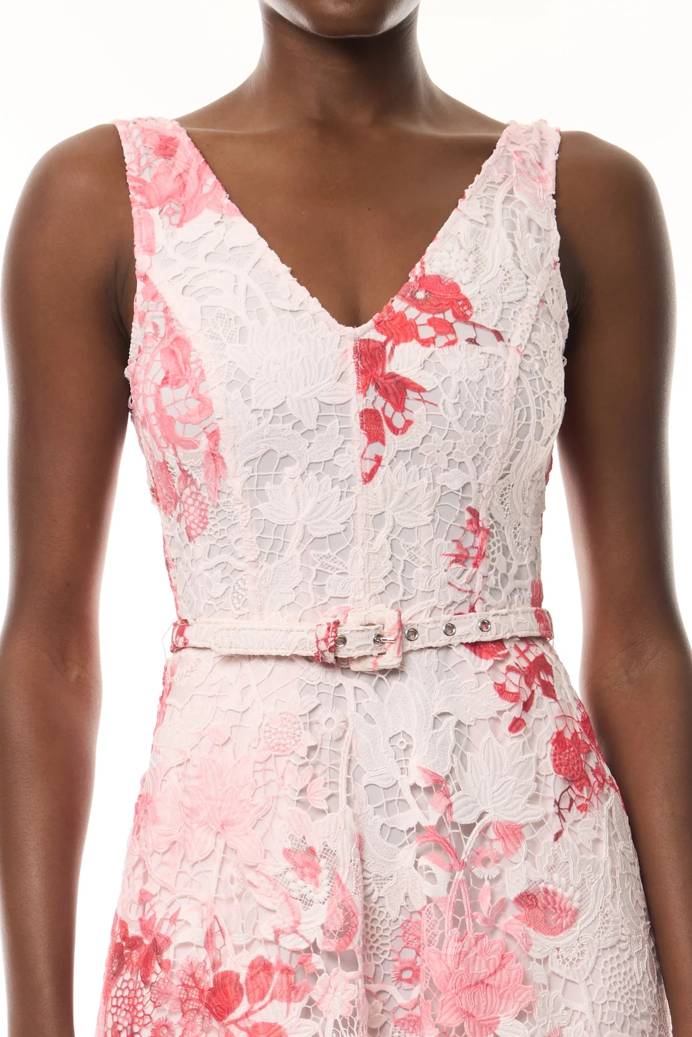 A person wears the Monique Lhuillier Rose Printed Lace Midi Dress—an elegant sleeveless white dress with pink and red floral patterns, crafted from guipure lace and finished with a matching waist belt.