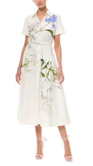 A woman wears the Monique Lhuillier Iris Printed Poplin Day Dress in Silk White, featuring short sleeves, button-down front, belted waist, and styled with strappy heeled sandals.