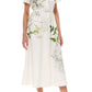 A woman wears the Monique Lhuillier Iris Printed Poplin Day Dress paired with white strappy high-heeled sandals.