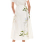 A woman stands facing away, wearing the Monique Lhuillier Iris Printed Poplin Day Dress in Silk White with short sleeves, collar, belted waist, and floral print, paired with white lace-up heels.