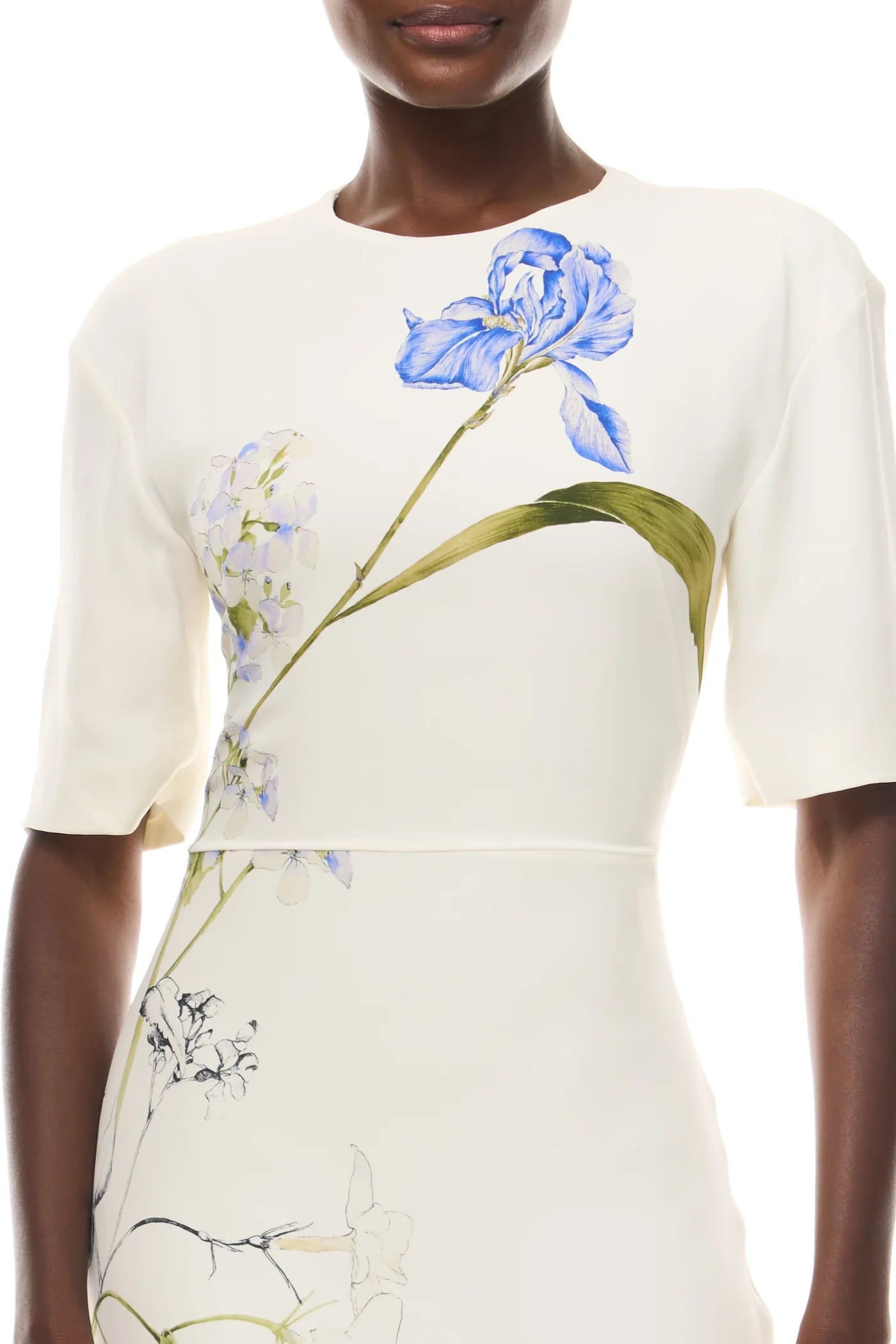 A person wearing the Monique Lhuillier Iris Bouquet Gown, an ivory multi short sleeve gown featuring a bold blue and green floral print reminiscent of an iris bouquet.