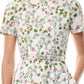 Someone wearing the Monique Lhuillier Ivy Bloom Short Sleeve Floral Day Dress, crafted from white stretch cotton poplin with a pink and green floral print and a coordinating fabric belt.