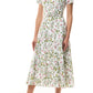 Woman wearing the Monique Lhuillier Ivy Bloom Short Sleeve Floral Day Dress—a white, midi-length stretch cotton poplin dress with pink and green floral print—paired with nude high-heeled sandals.