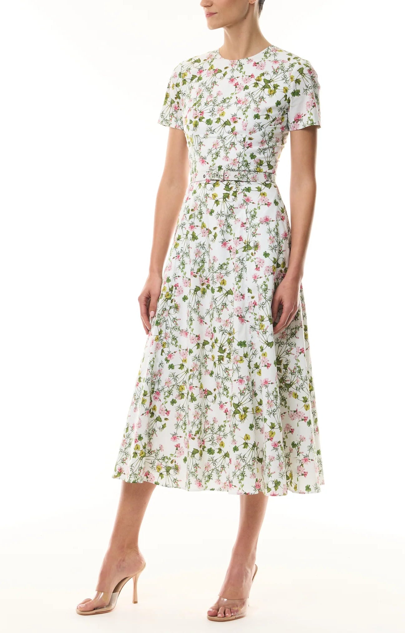 Woman wearing the Monique Lhuillier Ivy Bloom Short Sleeve Floral Day Dress—a white, midi-length stretch cotton poplin dress with pink and green floral print—paired with nude high-heeled sandals.