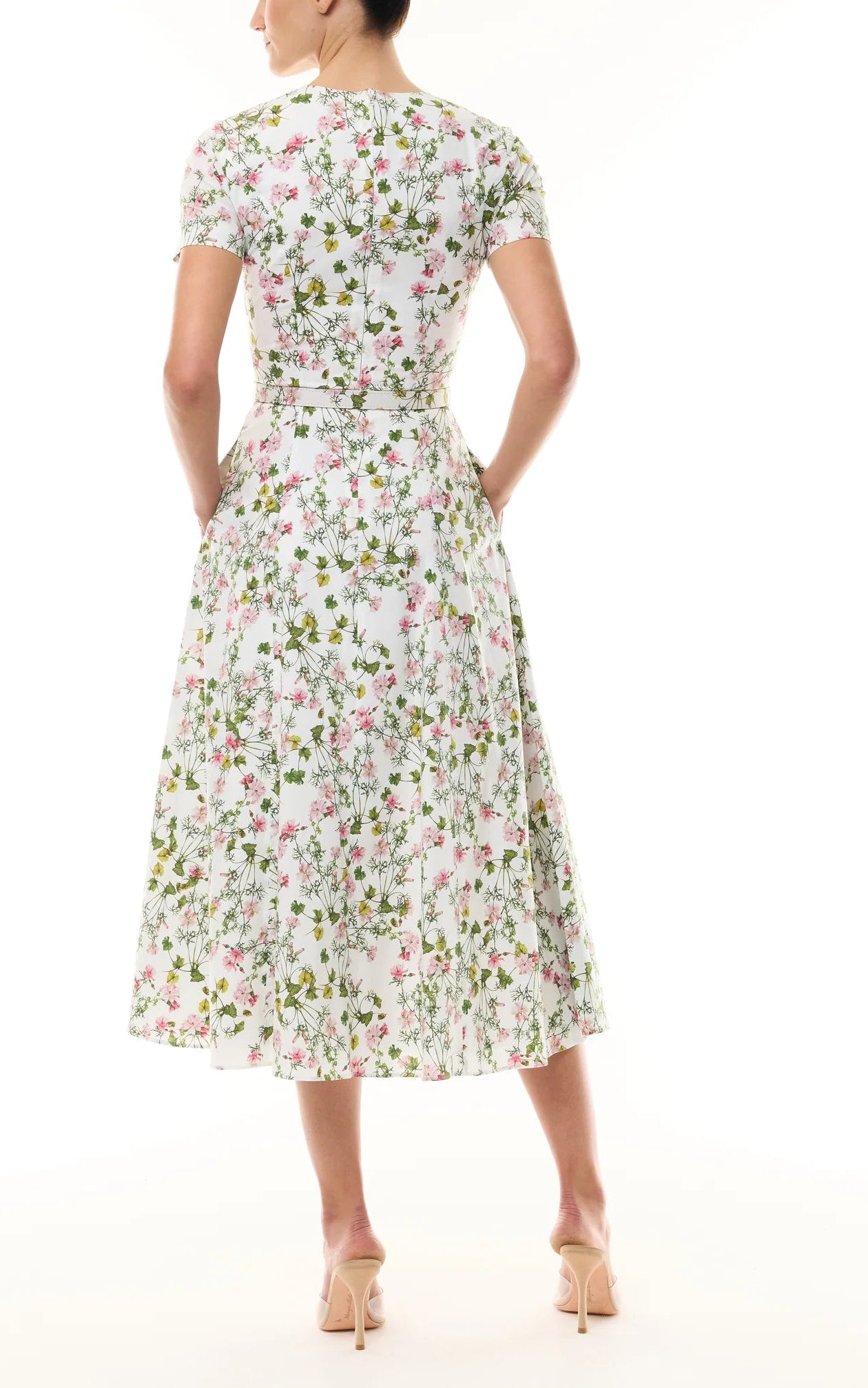 A woman stands with hands in pockets, wearing a Monique Lhuillier Ivy Bloom Short Sleeve Floral Day Dress and beige high heels.