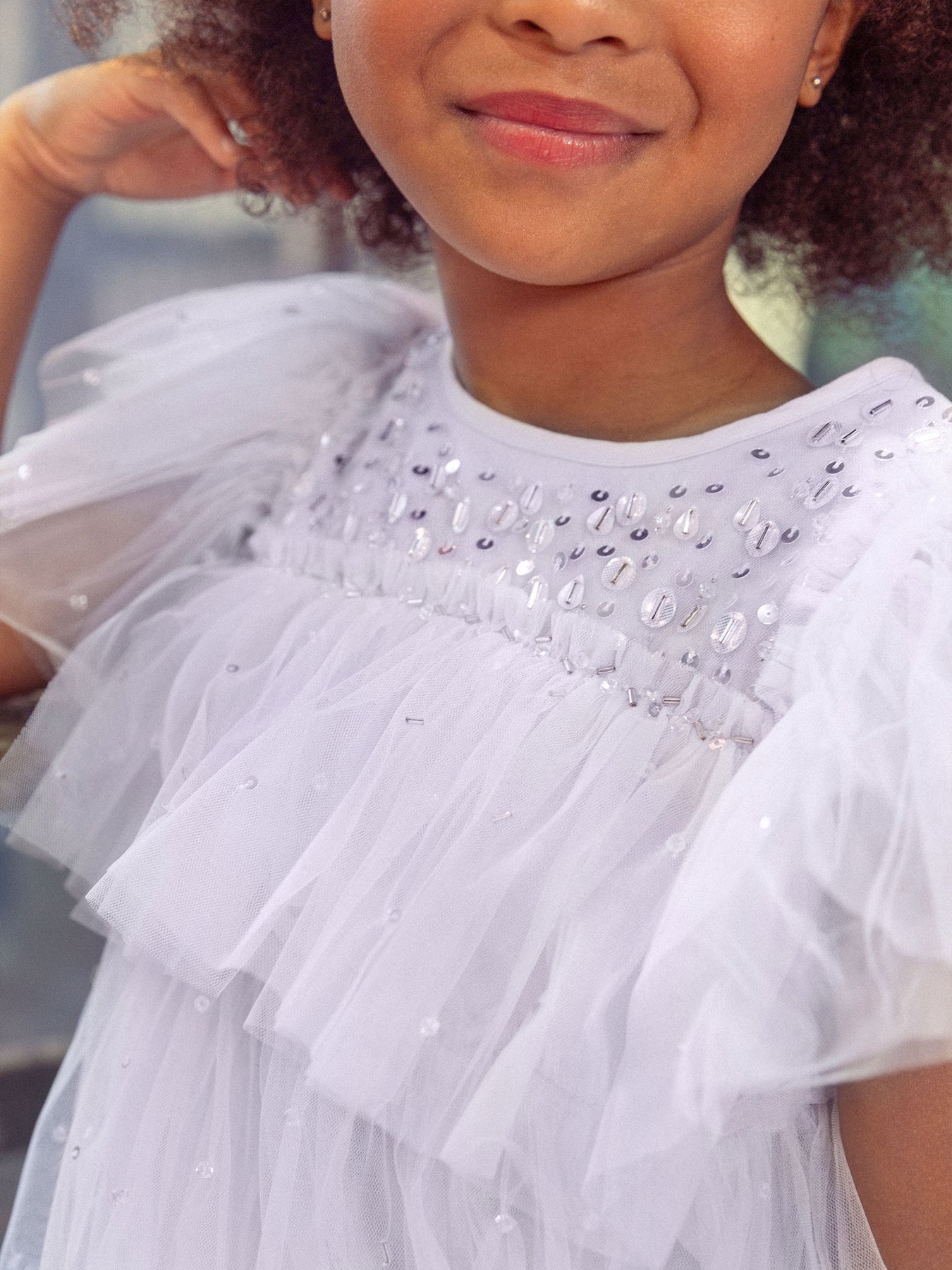 A child wearing the picture-perfect Girls’ Ziegfeld Tulle Dress by Tutu du Monde, featuring ruffled tulle sleeves and small bead embellishments near the neckline, smiles softly, exuding a touch of Hollywood magic.