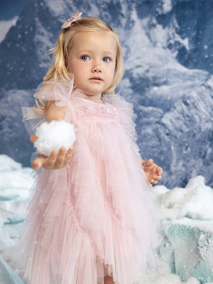 A young girl in a pale pink sparkle tulle Baby Girls’ Bébé Summit Sparkle Tulle Dress holds a snowball in a snowy landscape.