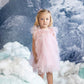 A young girl wears the Bébé Summit Sparkle Tulle Dress by Tutu du Monde, standing amid artificial snow with a snowy mountain backdrop.
