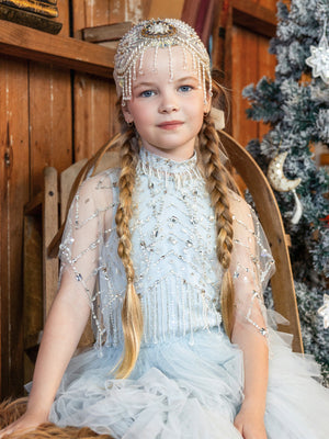 A girl wears the Tutu du Monde Girls’ Diamond Drift Cafe, a light blue dress with a crystal latticework capelet and a matching beaded headpiece.