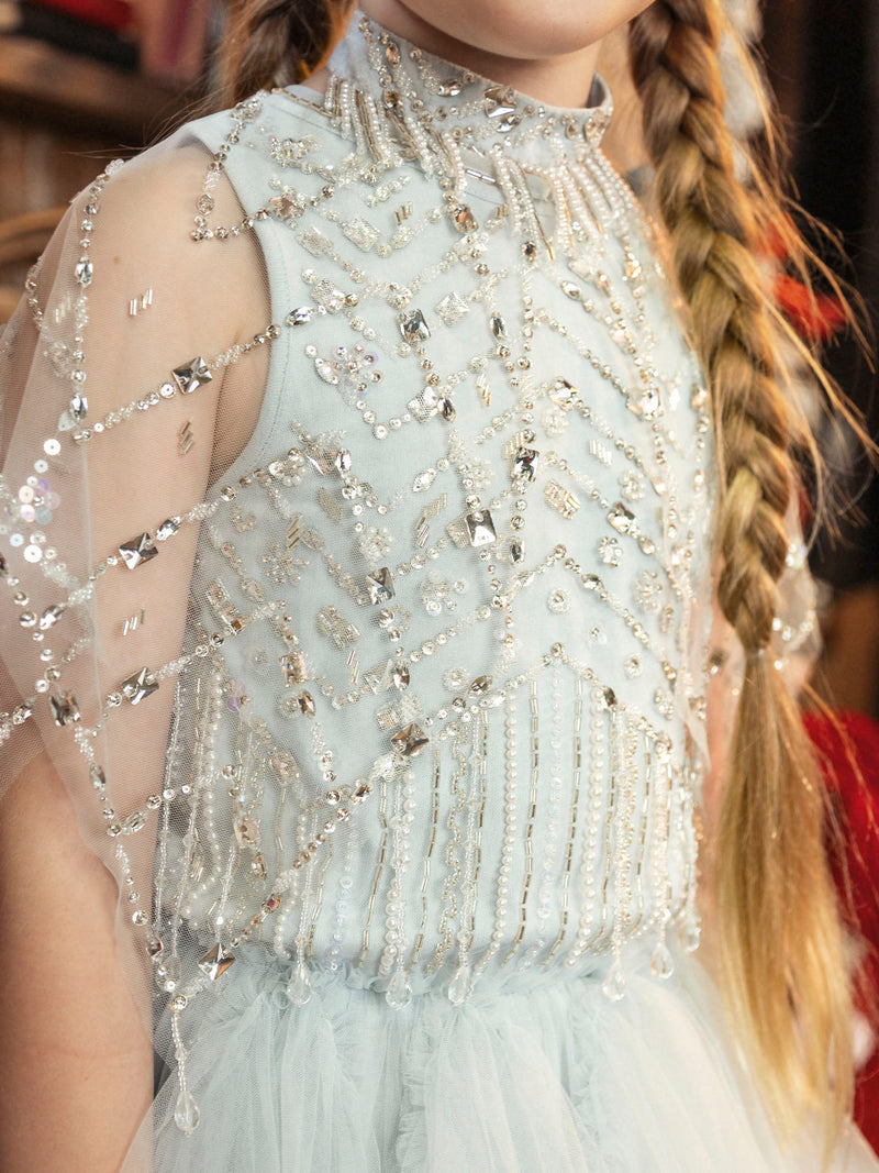 Child wearing a Diamond Drift Cafe dress by Tutu du Monde in Illusion Blue with beads, sequins, crystal latticework, and long braided hair draped over shoulders.