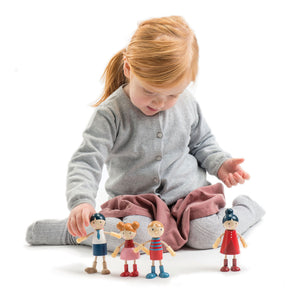 A young child sits cross-legged on the floor, arranging four Tender Leaf Toys Doll Family wooden dolls in front of them, set against a plain white background.