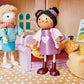 Two wooden dolls are seated in a charming dollhouse study, surrounded by Tender Leaf Toys' Doll House Study Furniture, which features a cozy cushioned couch, a leafy potted plant, framed wall art, and a cheerful yellow toy cat curled up in its pet bed—ideal pretend play accessories to enhance any children’s playset.