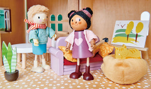 Two wooden dolls are seated in a charming dollhouse study, surrounded by Tender Leaf Toys' Doll House Study Furniture, which features a cozy cushioned couch, a leafy potted plant, framed wall art, and a cheerful yellow toy cat curled up in its pet bed—ideal pretend play accessories to enhance any children’s playset.