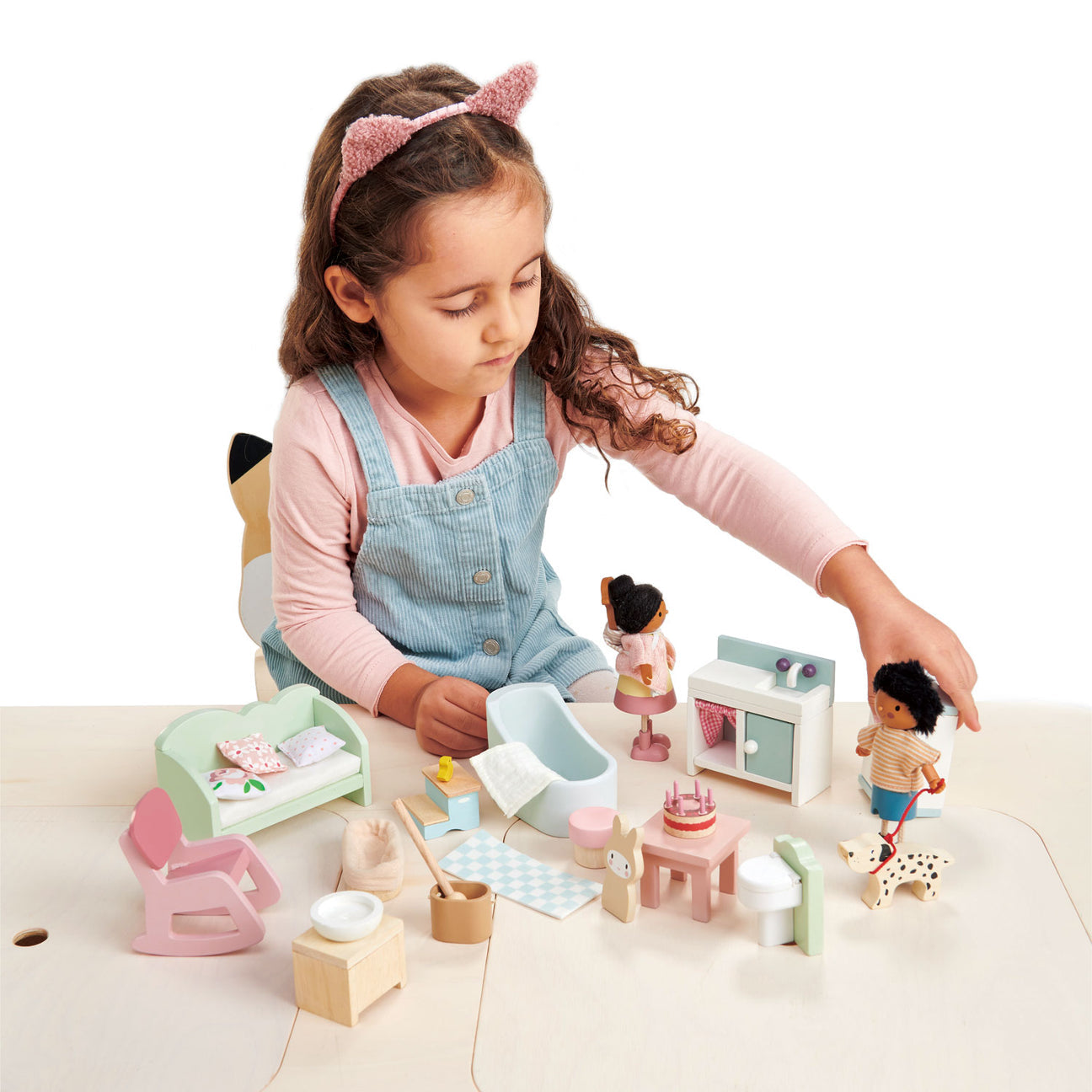 A young girl in a cat ear headband plays with the Countryside Furniture Set by Tender Leaf Toys, carefully arranging its miniature furniture and accessories on a light-colored table.