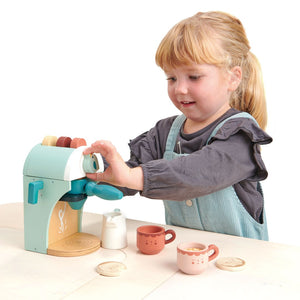 A little girl playing with a Tenderleaf Babyccino Maker by Tender Leaf Toys.