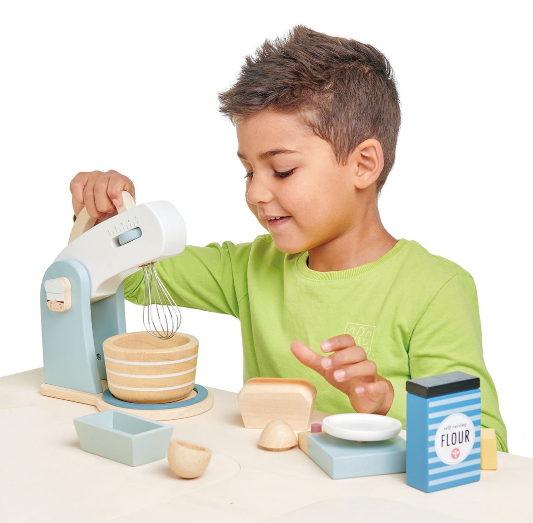 A young boy playing with a Tenderleaf Home Baking Set by Tender Leaf Toys in the kitchen.