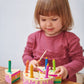 A little girl is playing with a Tenderleaf Rainbow Birthday Cake by Tender Leaf Toys.