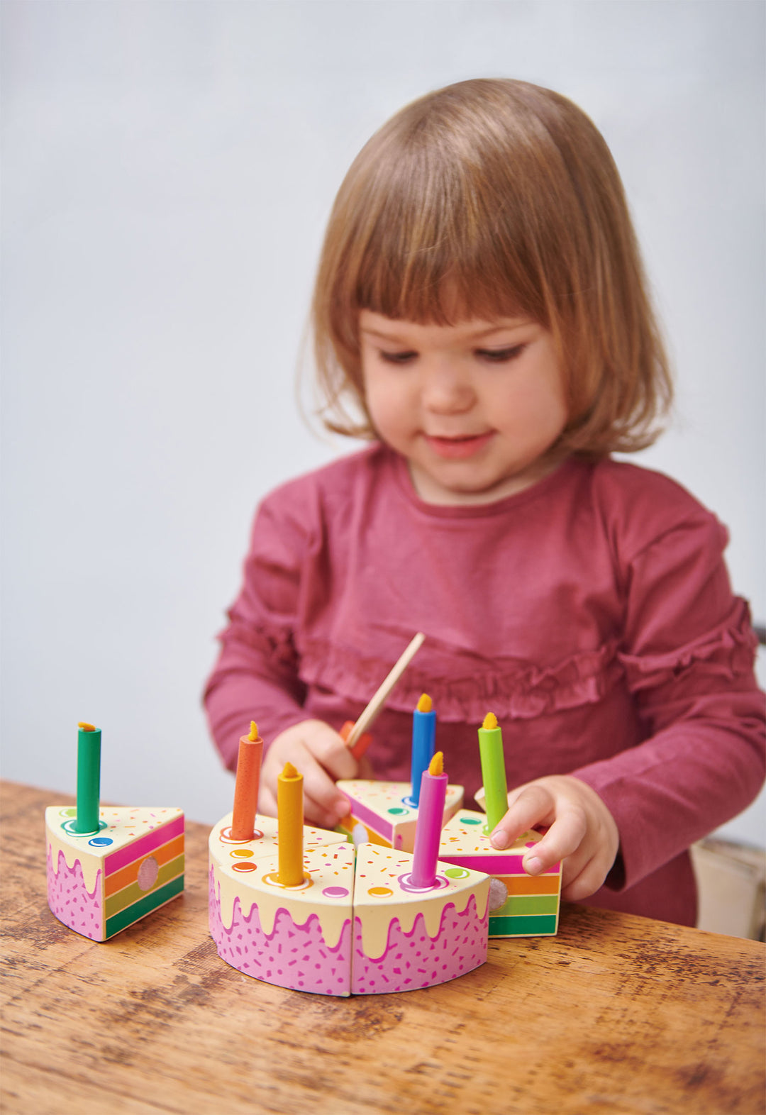 A little girl is playing with a Tenderleaf Rainbow Birthday Cake by Tender Leaf Toys.