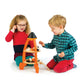 Two young children sit on the floor playing with the vibrant Tender Leaf Toys Cosmic Rocket Set, crafted from orange and natural wood. The girl wears glasses and a red dress, while the boy sports a blue plaid shirt and red pants.
