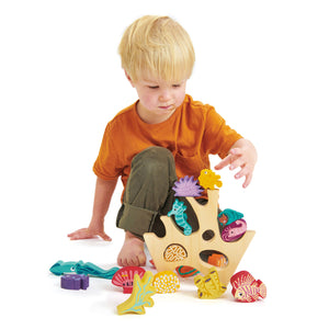 A young child in an orange shirt plays with the Stacking Coral Reef by Tender Leaf Toys, carefully placing colorful sea creatures onto the coral-shaped base for a delightful under-the-sea adventure.