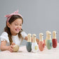 A young girl smiles as she prepares to roll a wooden ball toward a row of six colorful wooden skittles from her vibrant Birdie Skittles game by Tender Leaf Toys on the table.