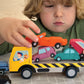 A child in a green shirt sits at a table, stacking the colorful Tender Leaf Toys Stacking Cars onto a yellow toy truck, enjoying a fun game that helps develop fine motor skills.