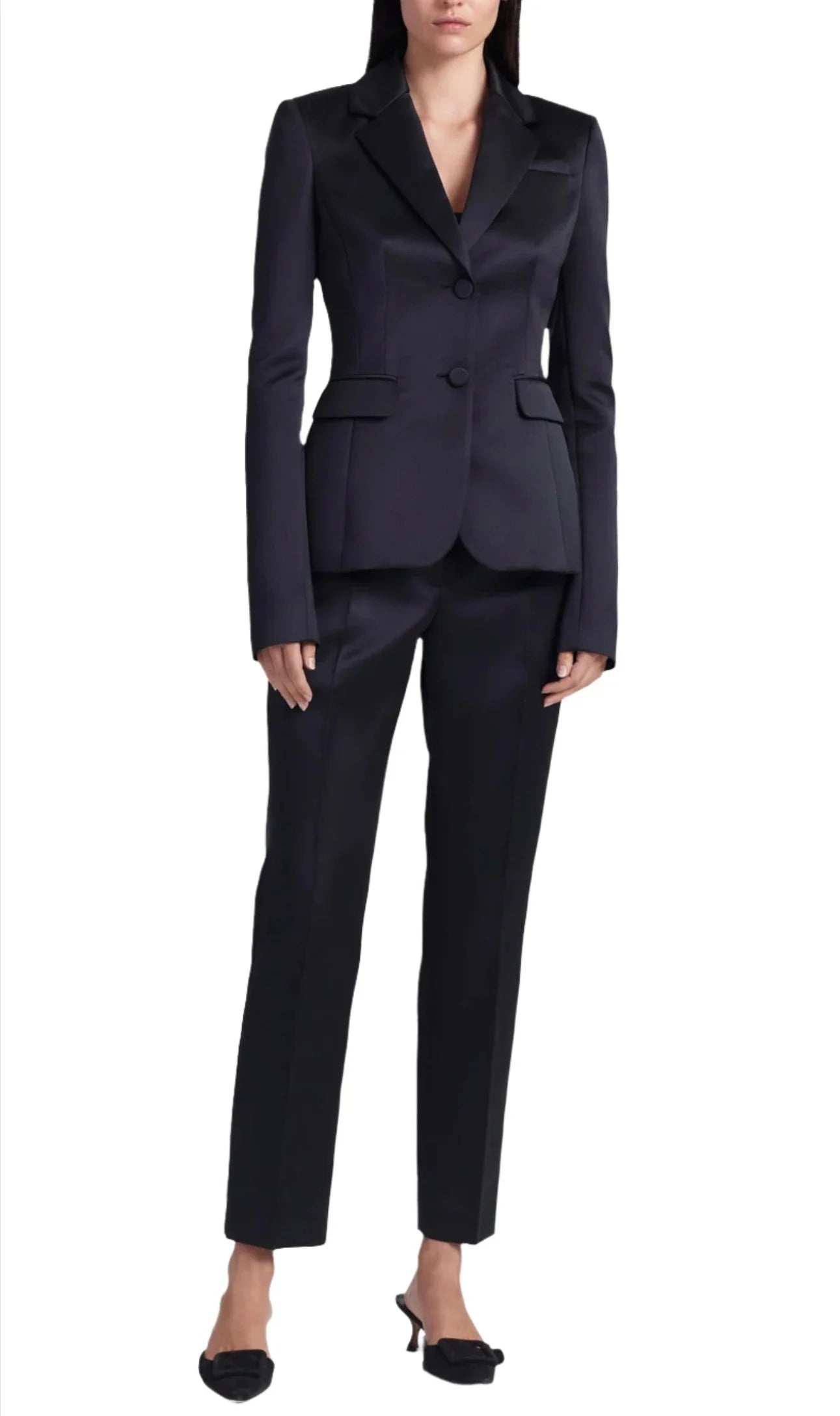 A person stands wearing a tailored black pantsuit with a blazer and matching mid-rise waist Altuzarra Todd Pant trousers, paired with black heels.