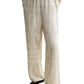 Someone wearing Toteme Monogram Silk PJ Bottoms—cream-colored trousers with black geometric line patterns—has hands in pockets and pairs them with a black top and black shoes.