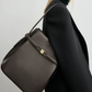A person in a black blazer and dark turtleneck carries a Toteme Belted Bucket Bag made from brown Palmellato leather with gold accents over their shoulder.