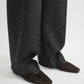 A person stands on a light-colored surface wearing dark gray wide-leg pants and Toteme’s Minimalist Suede Ballerinas, brown square-toe shoes made in Spain.