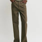 Wearing Toteme's Twisted Tailored Trousers—brown wide-leg style—paired with a beige long-sleeve top, this person stands hands in pockets, shown from shoulders down.