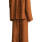 A person shown from the back wears Toteme's Monogram Silk PJ Top, a loose-fitting, rust-colored top with a geometric line pattern and silk twill texture.