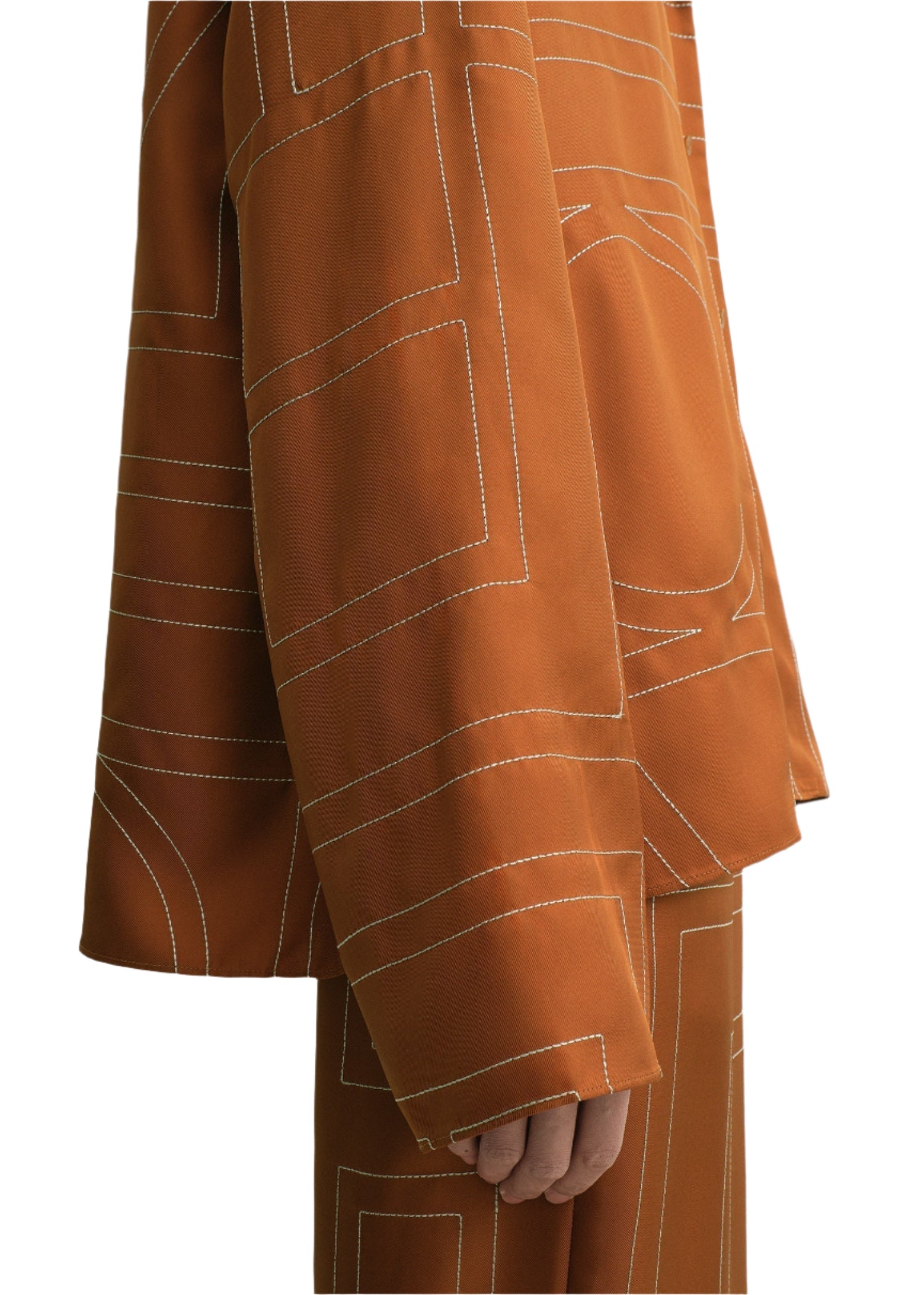 A person models the Toteme Monogram Silk PJ Top in orange, featuring white geometric stitching and a subtle monogram pattern, shown from shoulder to knee against a white background.