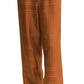 Someone wearing Toteme's Monogram Silk PJ Bottoms—rust-colored silk twill pants with a geometric stitched pattern—paired with black sandals and a white top draped over their shoulders.