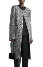A person wears the Toteme Collarless Floral Coat in black and white over a black top and pants, accessorized with a small black handbag—a chic outfit for any occasion.